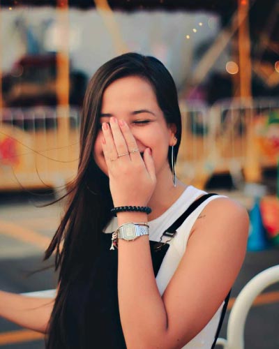 A photo of a beautiful woman smiling with her hand slightly covering her face