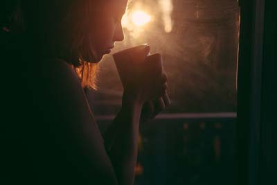 A photo of a woman holding a cup of coffee while contemplating about something